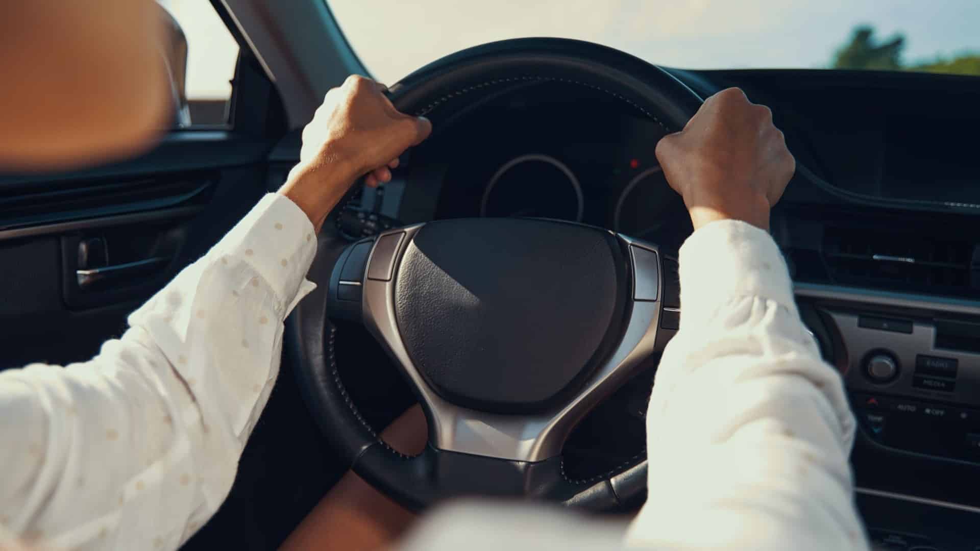 Person putting two hands on upper part of black wheel while driving a car