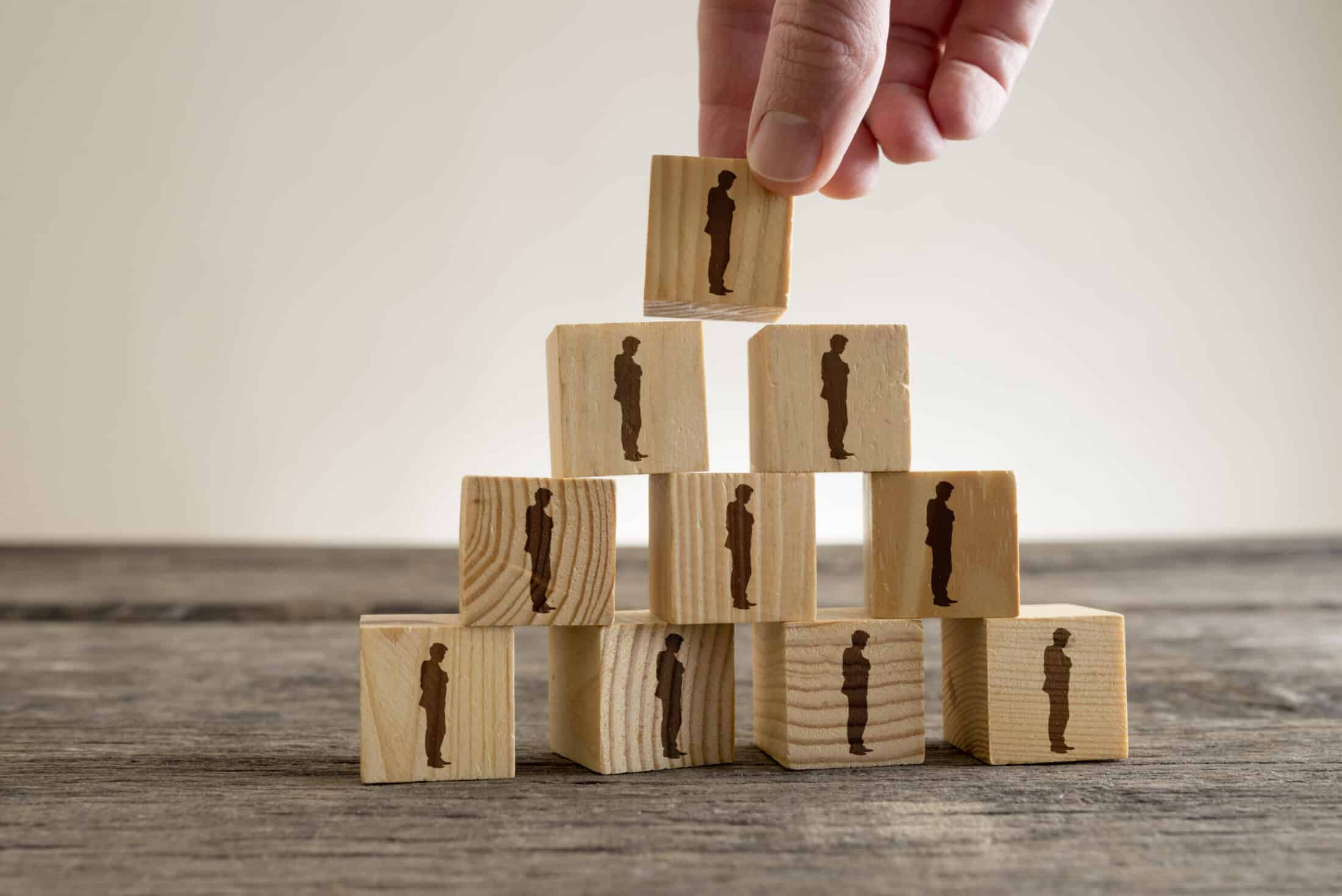 A man stacking a tower of wood blocks with human silhouettes, human resources and management concept.